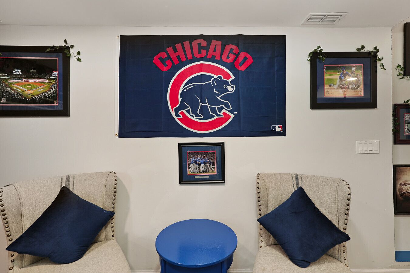 Une pièce décorée d’une grande bannière des Chicago Cubs, de deux fauteuils avec des coussins bleus, d’une petite table bleue et de divers objets de collection sur le thème du sport, encadrés et accrochés aux murs.