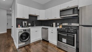 Une cuisine moderne avec des meubles blancs, un réfrigérateur en acier inoxydable, un four à micro-ondes, une cuisinière et un lave-linge.