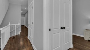 Un couloir avec des portes blanches, une rambarde blanche et un plancher en bois.