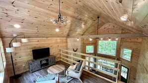 A cozy cabin interior with a wooden ceiling, a television, a sofa, and a dining area.