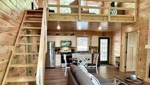 A cabin interior with a loft bedroom, a kitchen, and a living area with a sofa and a dining table.