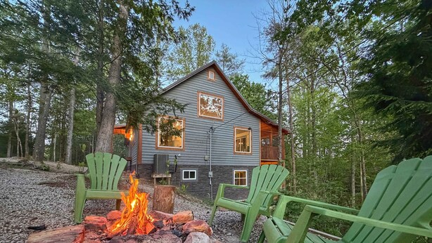 Eine Holzhütte mit Feuerstelle und grünen Adirondack-Stühlen.