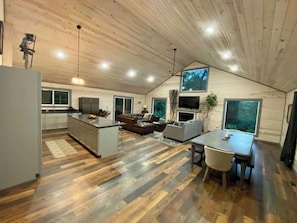 Um interior moderno com cozinha, sala de jantar e sala de estar, apresentando pisos de madeira e teto inclinado.