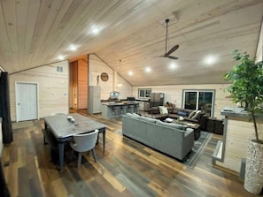 A spacious living area with a dining table, grey sofa, and a kitchen in the background.