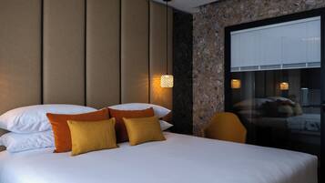 A hotel room with a large bed, multiple pillows, a sofa, and a large window with blinds.