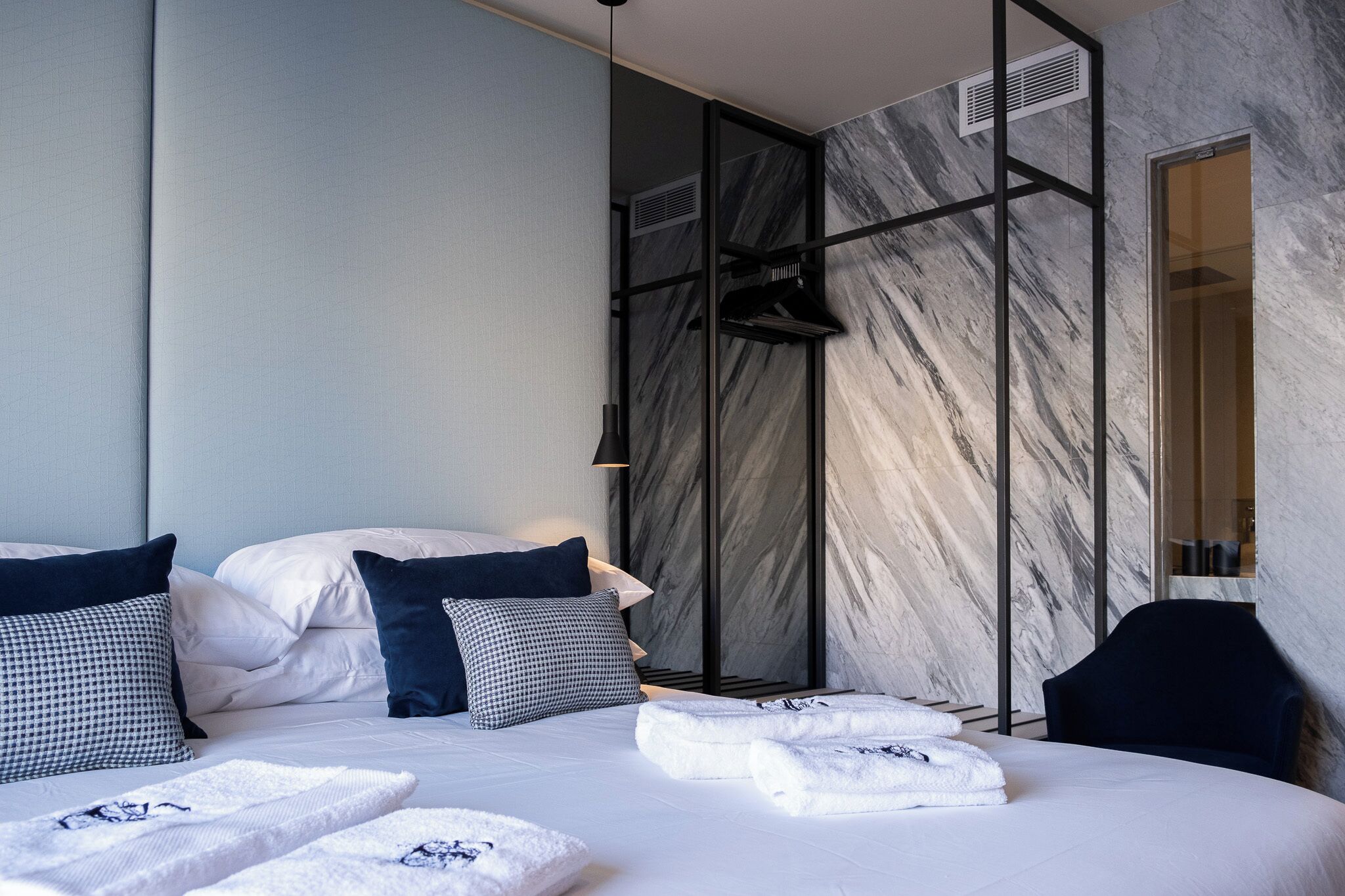 A modern hotel room with a large bed, a seating area, and a marble wall.
