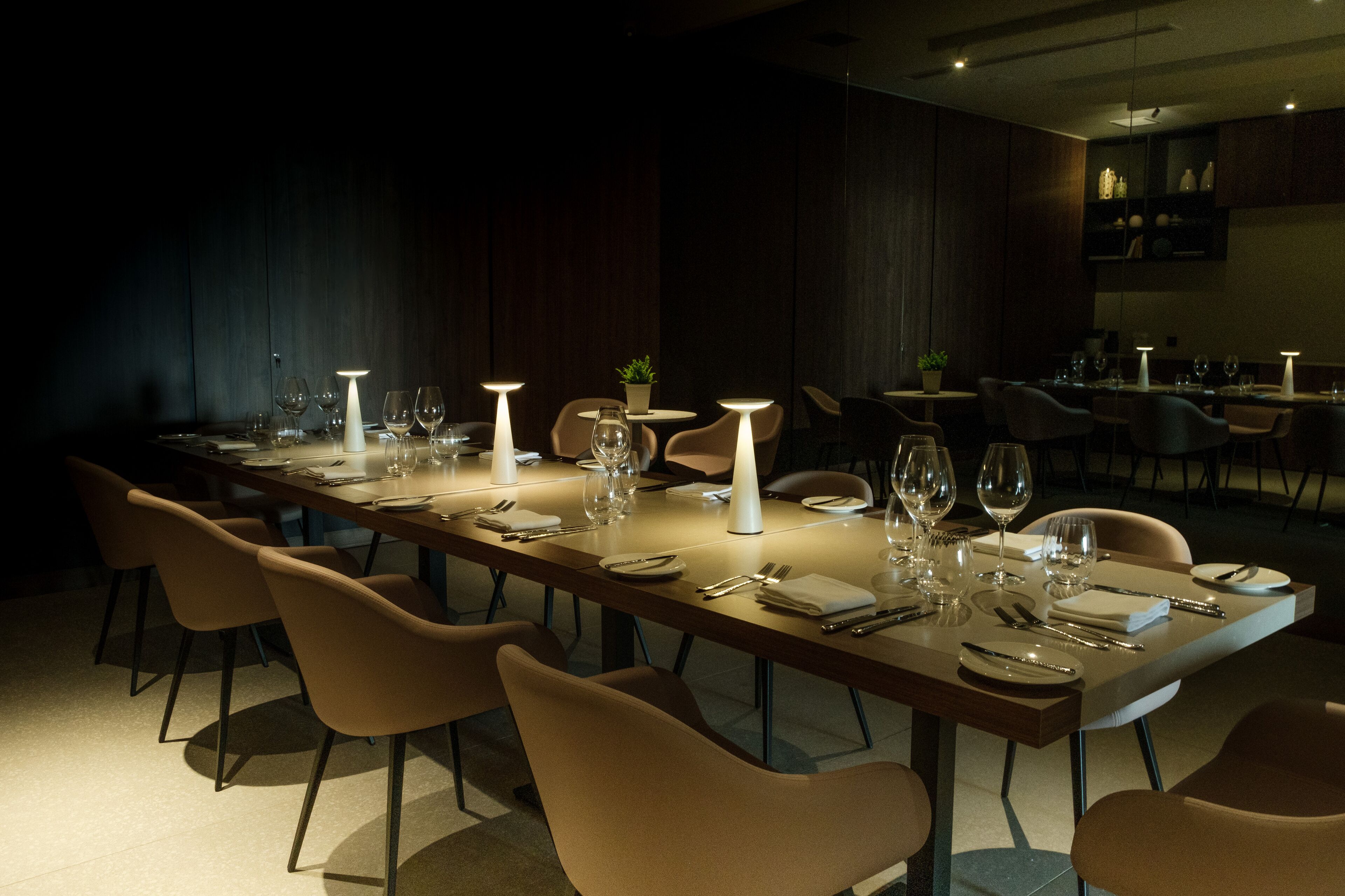 A long dining table set with chairs, candles, and dinnerware in a dimly lit room.