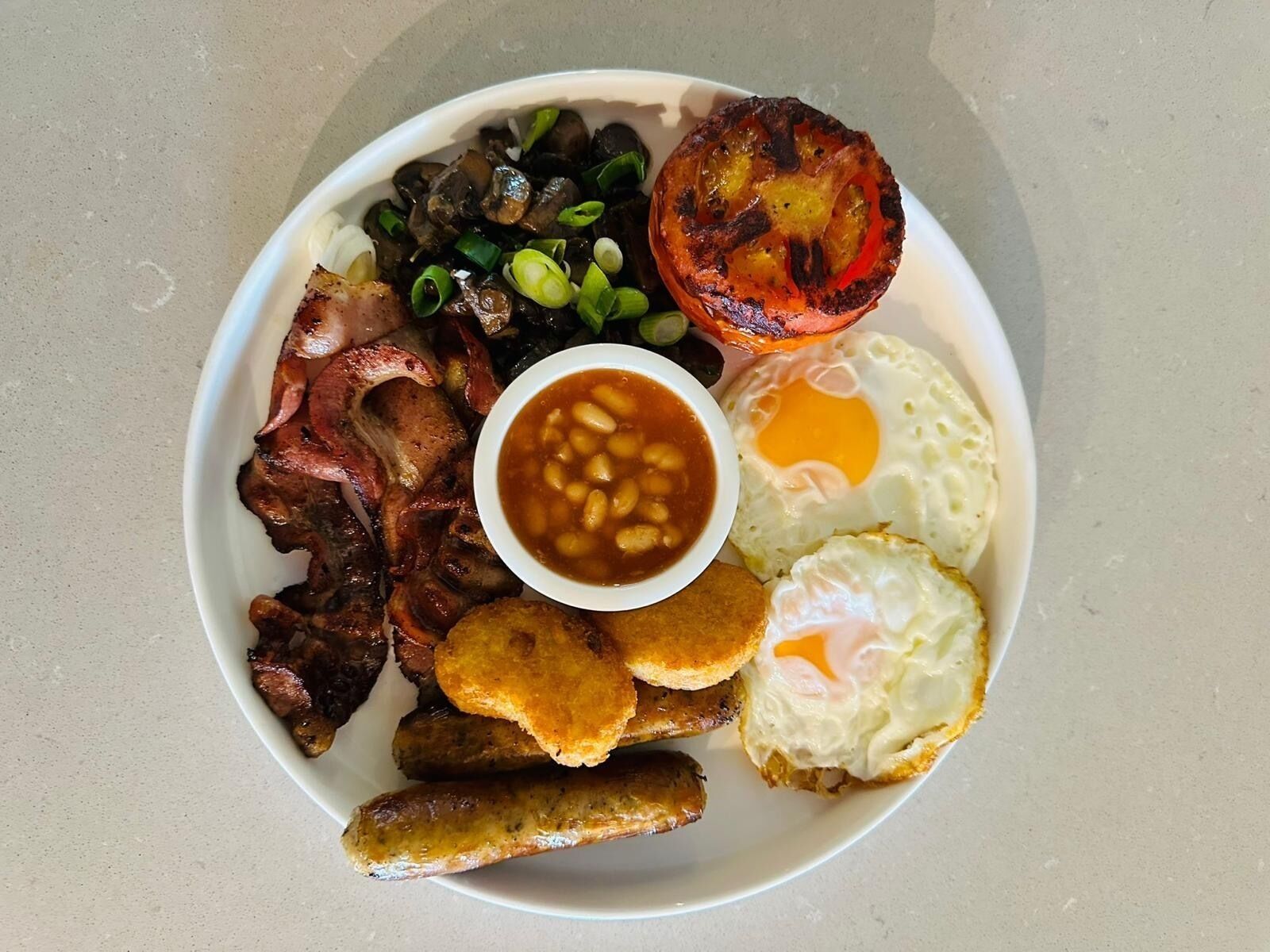 En tallrik med olika frukosträtter, inklusive bacon, ägg, bönor och en grillad tomat.