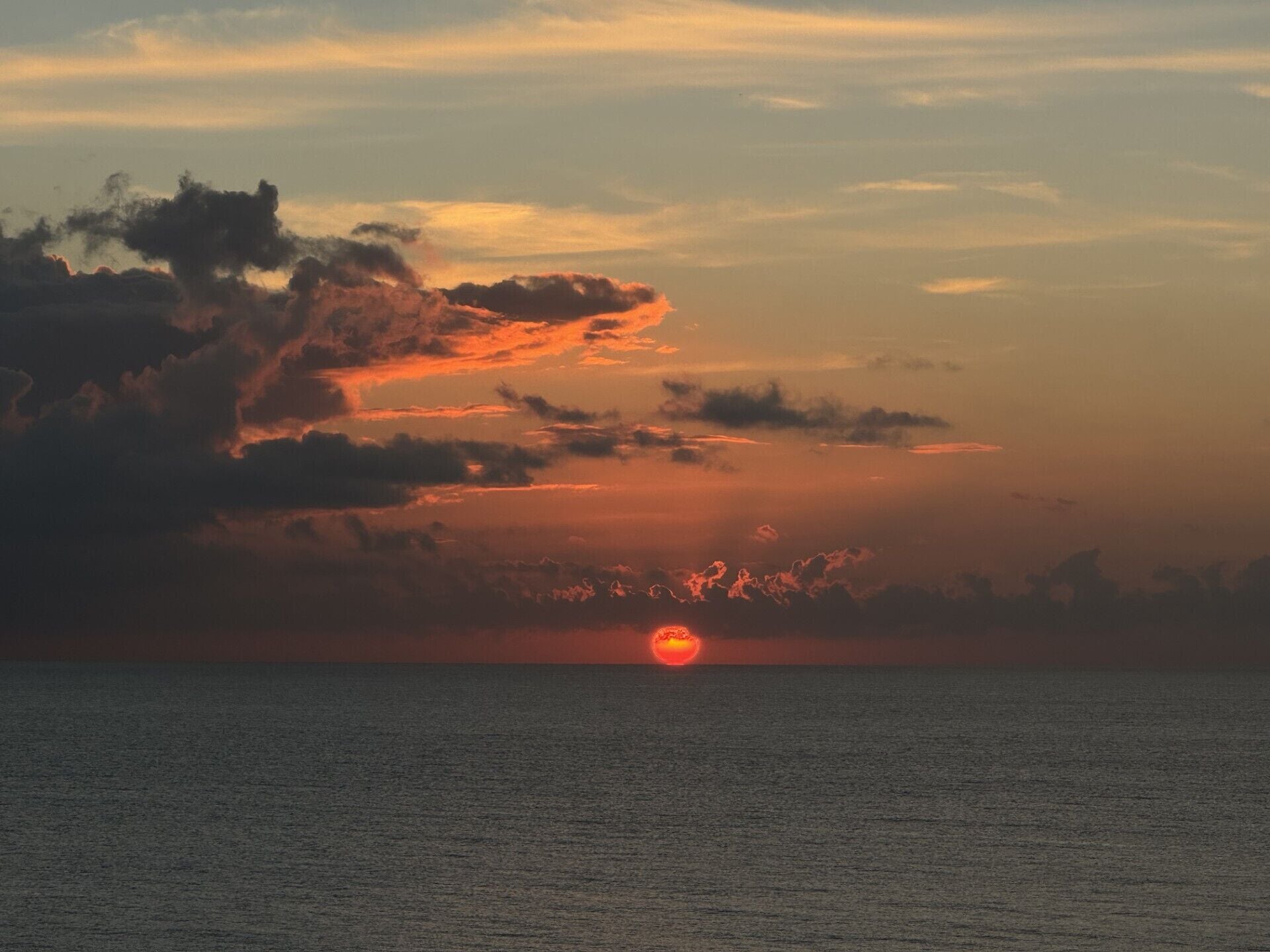 Un sol ponent-se sobre un mar tranquil amb núvols al cel.
