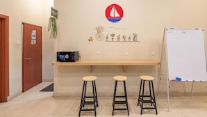 A reception area with a wooden counter, three stools, a whiteboard, and a sign indicating a toilet. - Harbour Hotel (Petaling Jaya)