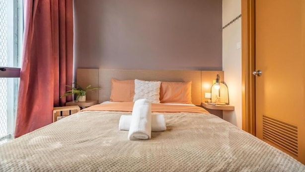A neatly made bed with a rolled towel, a bedside table with a lamp, and a window with curtains. - Harbour Hotel (Petaling Jaya)
