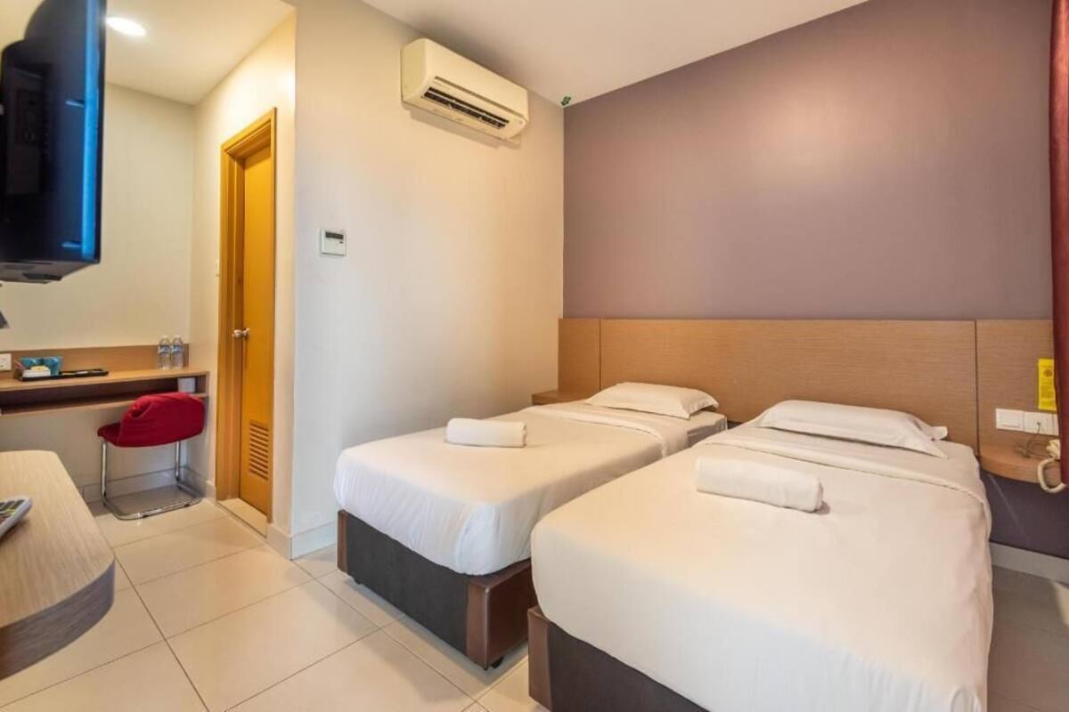 A hotel room with two beds, a desk, a chair, an air conditioning unit, and a television.