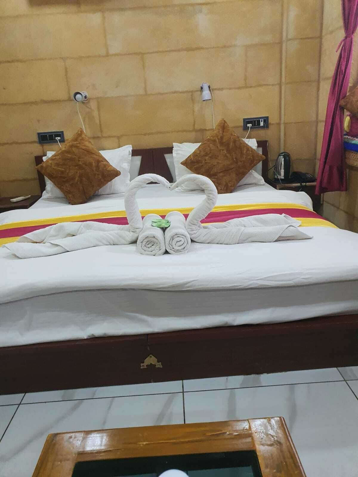 A hotel room with a bed, pillows, and a towel arrangement forming a heart shape.