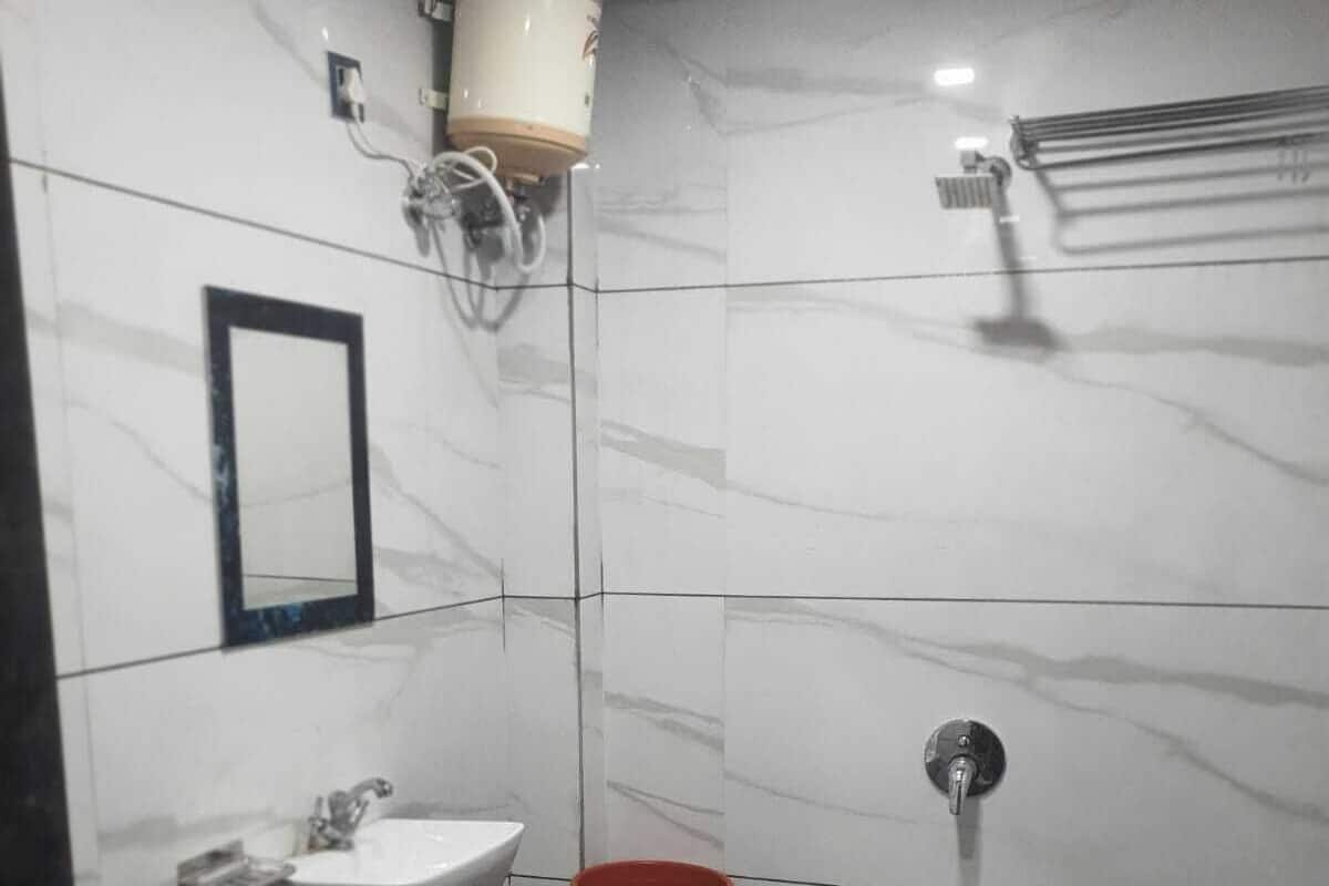Ein Badezimmer mit einem weißen Waschbecken, einem Spiegel, einer Toilette, einem roten Eimer und einem blauen Hocker.