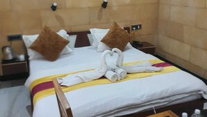 Une chambre d’hôtel comprenant un lit, des oreillers, une table de chevet, une commode, un appareil de climatisation et une petite table avec des bouteilles d’eau.