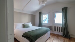 A bedroom with a bed, a window with curtains, a radiator, and a wooden floor. - Mansarda Verde (Tresa)