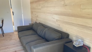 Een moderne woonkamer met een grijze bank, houten vloeren en een wand bekleed met hout.