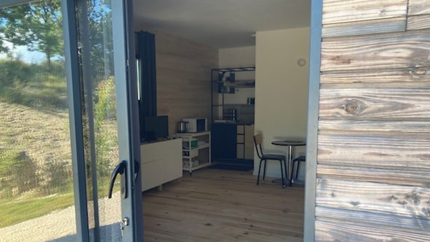 Een modern interieur met een houten vloer, een keuken met kasten en apparatuur, een eettafel met stoelen en een glazen schuifdeur naar een buitenruimte.