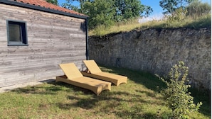 Een houten hutje met een rood pannendak, een klein raam en twee beige loungestoelen in de tuin.