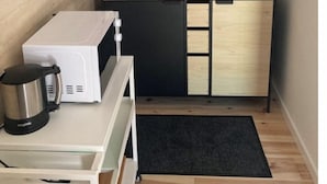 Een kleine keuken met een magnetron, waterkoker en opbergkasten.