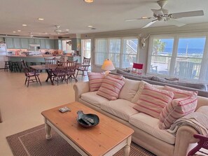 A spacious living area with a sofa, coffee table, and dining table. A kitchen is visible in the background. - Faye DoDo - Beachfront - Island Realty (Grand Isle)