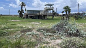 A two-story building with a balcony on the upper floor, surrounded by open fields and palm trees. - Faye DoDo - Beachfront - Island Realty (Grand Isle)