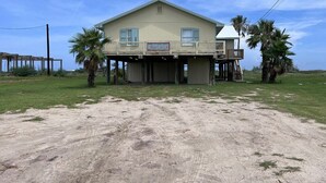 A two-story house with a balcony, a sign reading "Beach House," and a sandy ground in front. - Faye DoDo - Beachfront - Island Realty (Grand Isle)