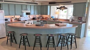 A kitchen with a central island, bar stools, and teal cabinetry. - Faye DoDo - Beachfront - Island Realty (Grand Isle)