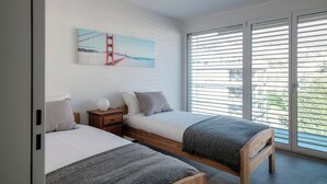 Een slaapkamer met twee bedden, een nachtkastje, een schilderij van de Golden Gate Bridge en een grote schuifpui naar buiten.