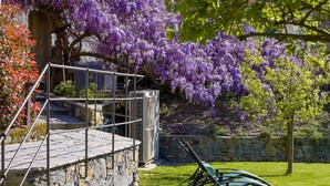 Eine Steinsäule mit Metallgeländer, eine Rasenfläche und blühende, violette Bäume.