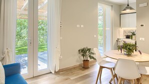 Ein modernes Wohnzimmer mit einem blauen Sofa, einem runden Esstisch mit weißen Stühlen und einer Topfpflanze.