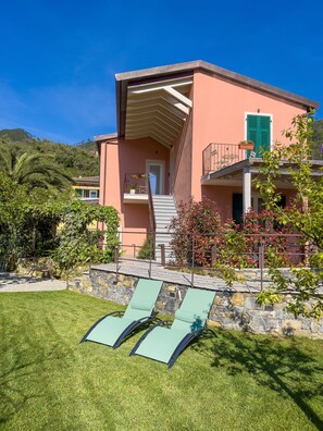 A two-story building with a balcony, a stone wall, and a grassy lawn with sun loungers. - "MAGNOLIA" - Apartment on the ground floor, with veranda. (Levanto)