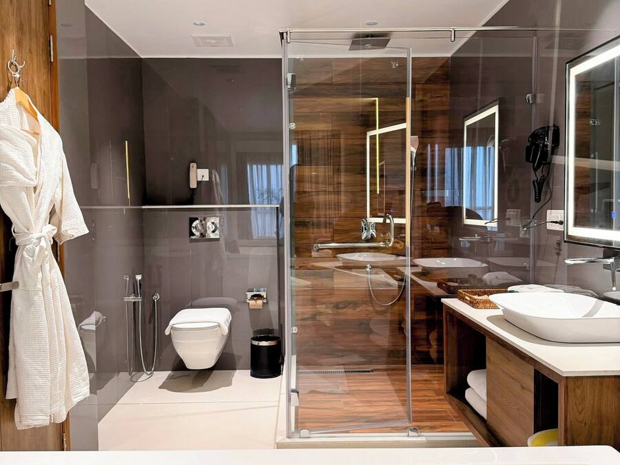 A modern bathroom with a glass-enclosed shower, a white bathtub with rose petals, and a wooden vanity with a mirror.