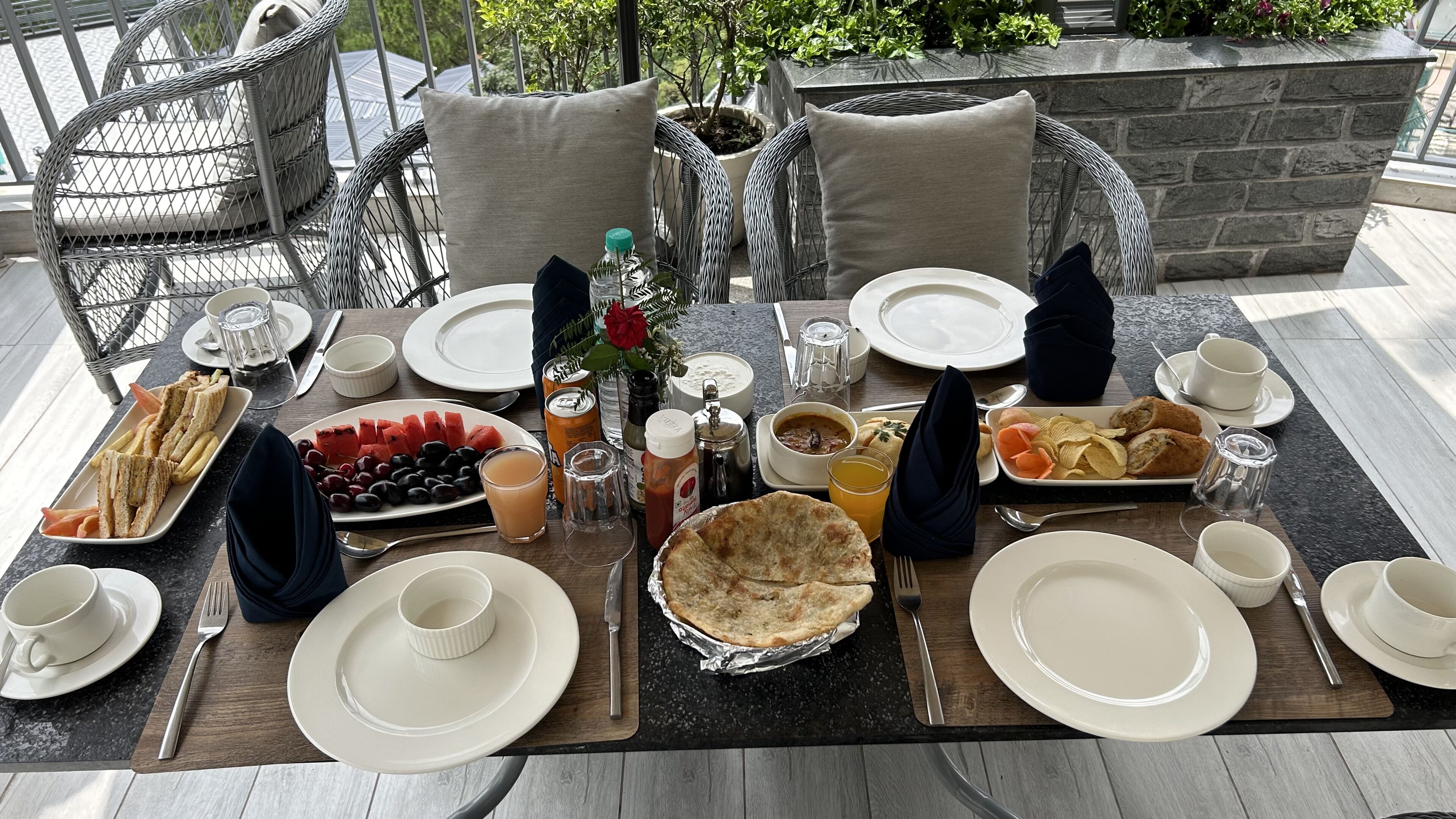 Une table dressée pour un repas, avec des assiettes, des couverts et différents plats, notamment des sandwichs, des fruits et une tarte.