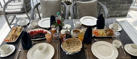 Une table dressée pour un repas, avec des assiettes, des couverts et différents plats, notamment des sandwichs, des fruits et une tarte.