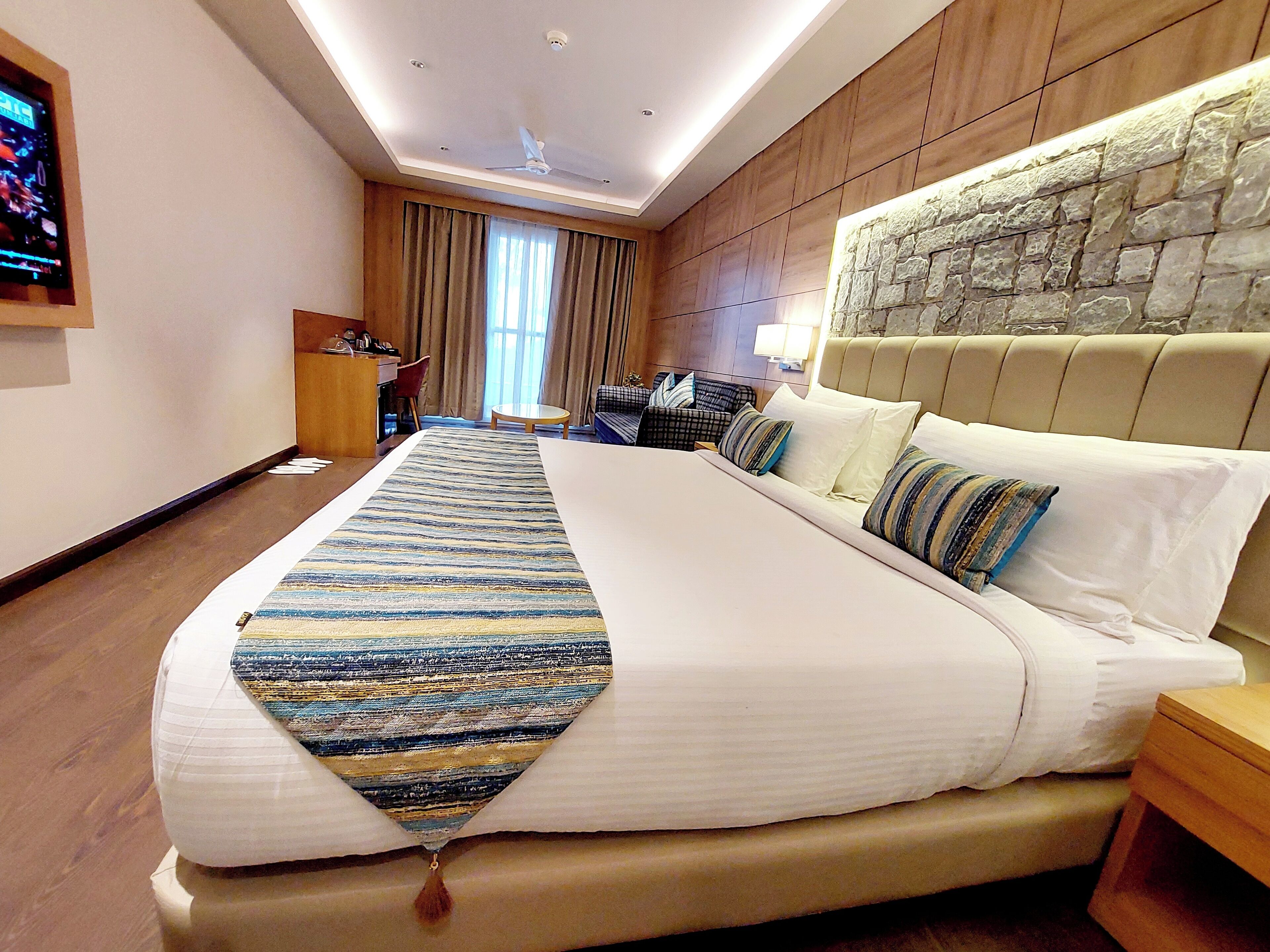 A hotel room with a large bed, a desk, a chair, and a stone accent wall.