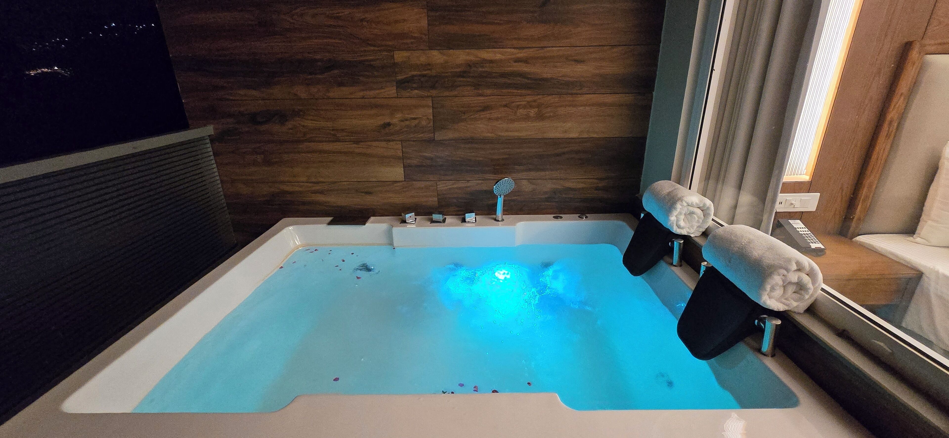A modern bathroom with a large bathtub, wooden wall panels, and a window with curtains.