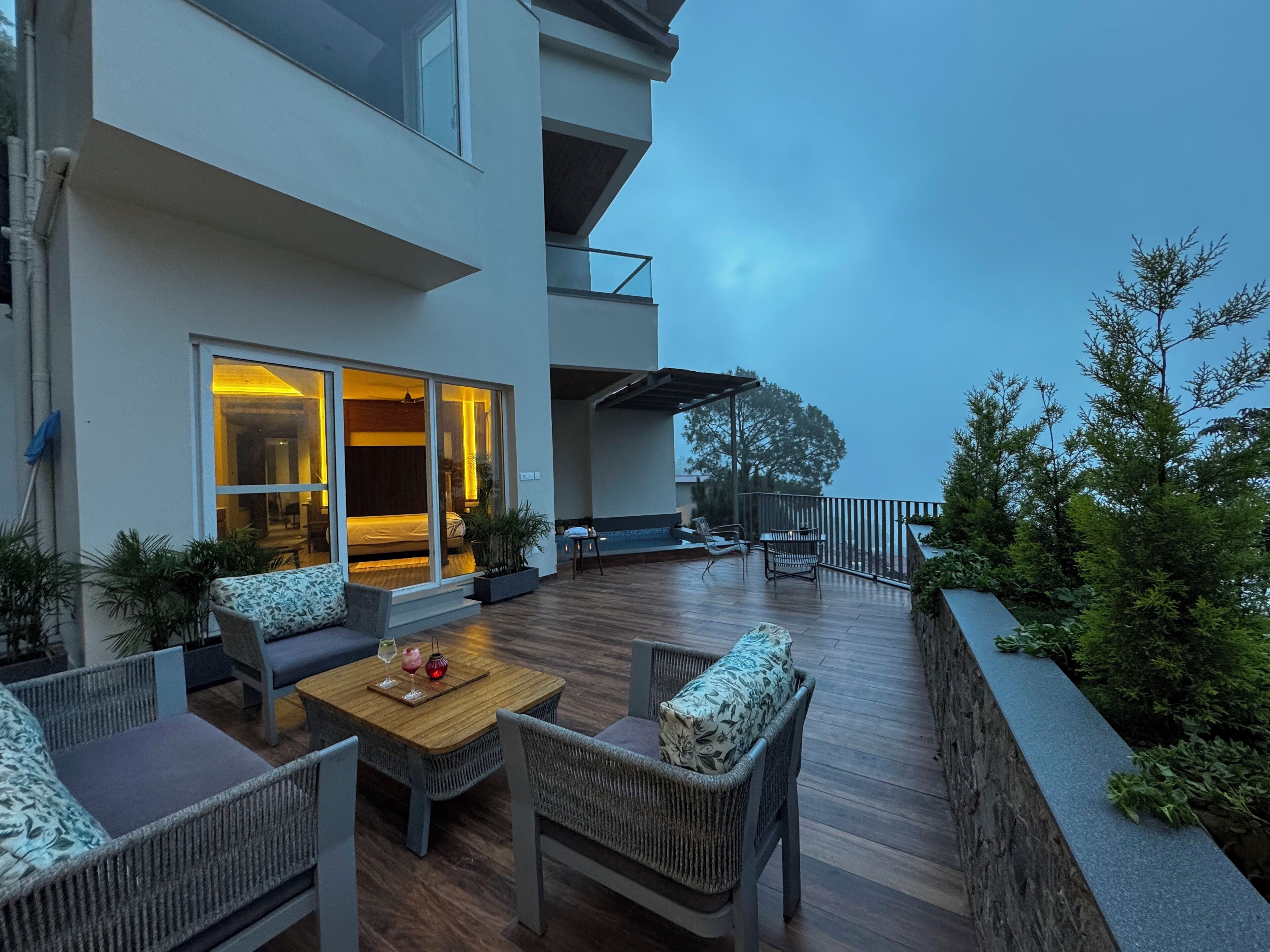 A modern outdoor patio with wicker furniture, a wooden table, and a glass door leading to an interior room.