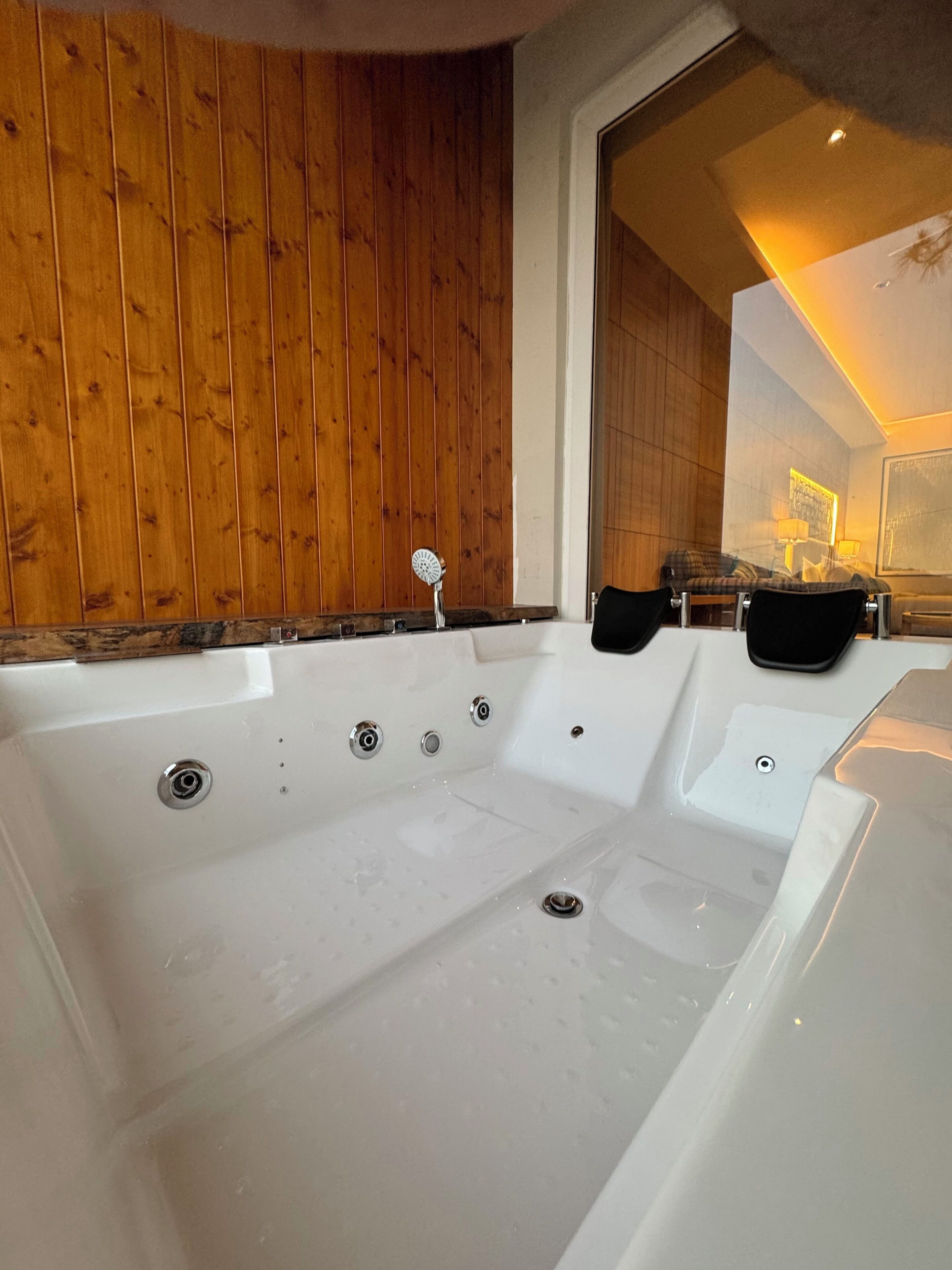 A large white bathtub with multiple faucets, wooden paneling on the walls, and a seating area with a sofa and armchairs.