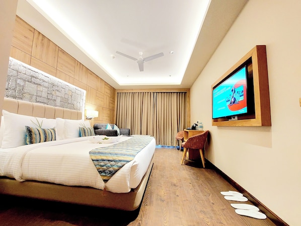 Habitación de hotel con una cama grande, televisor, escritorio y una silla.