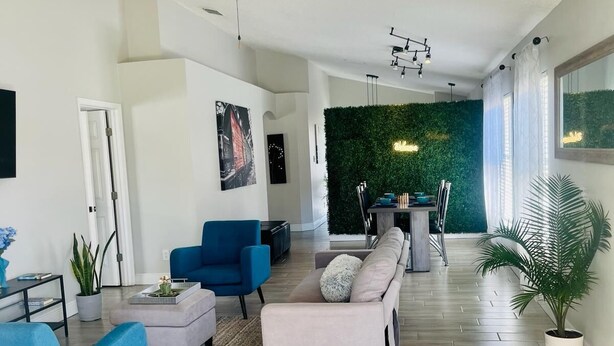 Ein großzügiges Wohnzimmer im modernen Stil, mit Deckenventilator, Essbereich mit grüner Wand und einem großen Fenster für natürliches Licht.