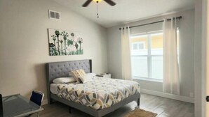 Ein Schlafzimmer mit einem Bett, einem Schreibtisch, einem Deckenventilator und einem Fenster mit Vorhängen.