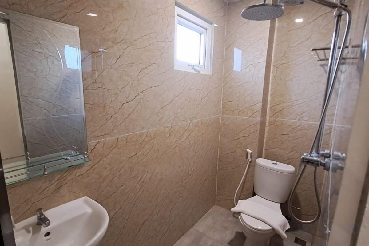 Ein Badezimmer mit Marmorwand, einer Glasablage, einem Waschbecken, einer Toilette und einer Dusche.