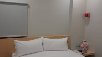 Una habitación de hotel con una cama bien hecha, un cabecero de madera, una mesita de noche con una lámpara roja y una lámpara de pared.