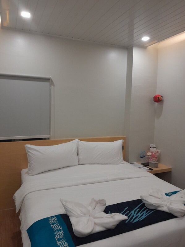 Ein Hotelzimmer mit einem ordentlich bezogenen Bett, einem Holzkopfende, einem Nachttisch mit einer roten Lampe und einer wandmontierten Leuchte.