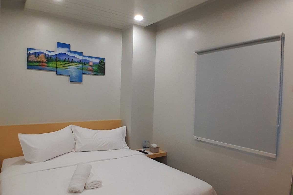 A hotel room with a bed, white linens, a headboard, a nightstand, a painting on the wall, and a whiteboard.