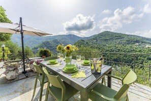 Une table installée à l’extérieur, avec une vue sur les montagnes, des chaises vertes et un parasol.