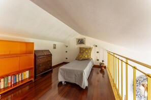 Une chambre à coucher avec un lit, une commode en bois, une bibliothèque et un escalier doté d’une rampe jaune.
