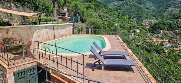 Une piscine sur le toit, avec une terrasse en pierre, un petit kiosque et une vue sur un village perché sur une colline.