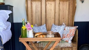 A cozy room with a wooden headboard, a small table with a bottle, flowers, and pastries. - Shepherd Hut in Private Meadow With Outdoor Bath (Langport)
